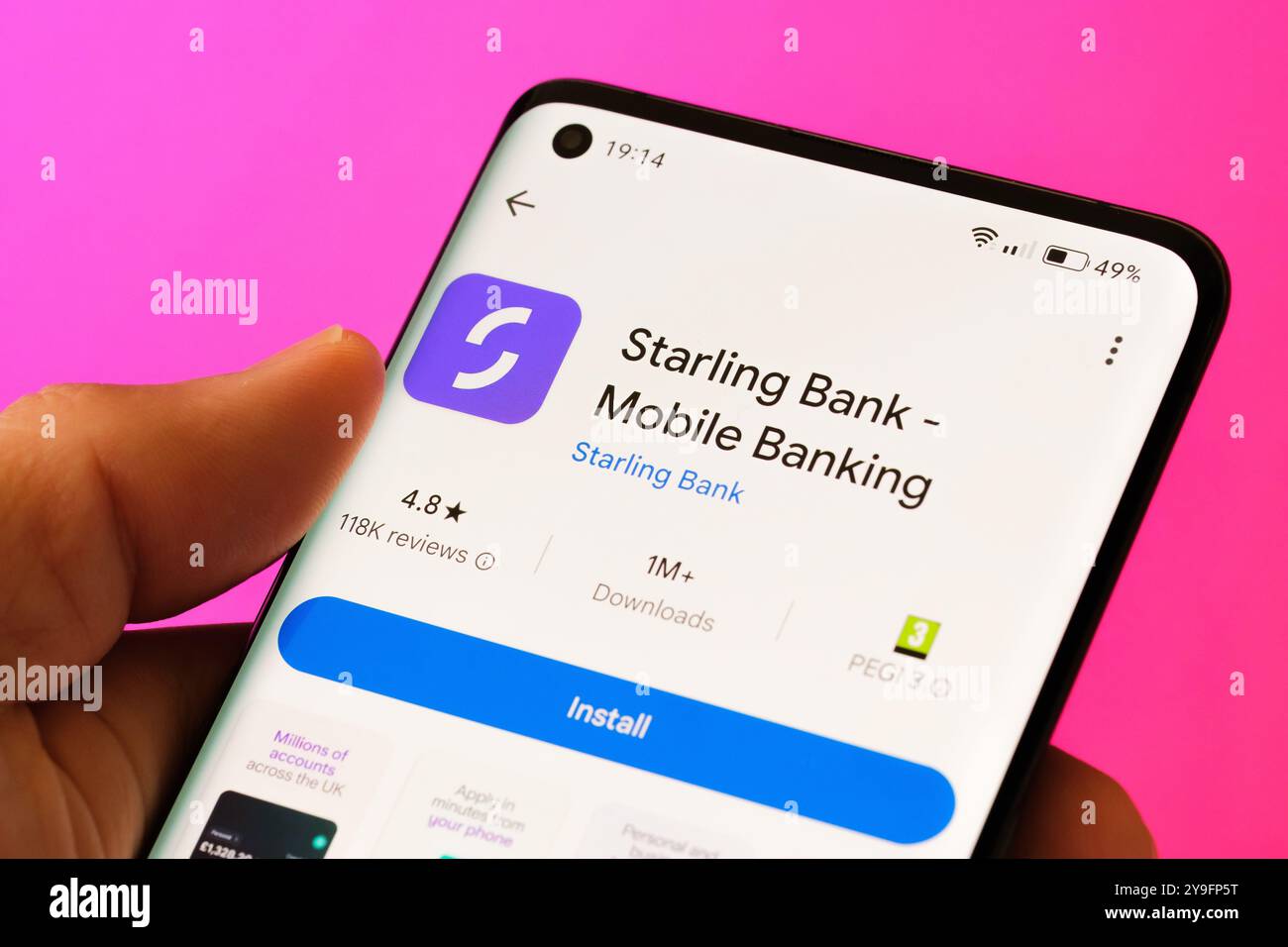 Primo piano di una mano che tiene in mano uno smartphone e visualizza la schermata di installazione dell'app per il mobile banking di Starling Bank. Sfondo rosa. Stafford, Regno Unito Foto Stock