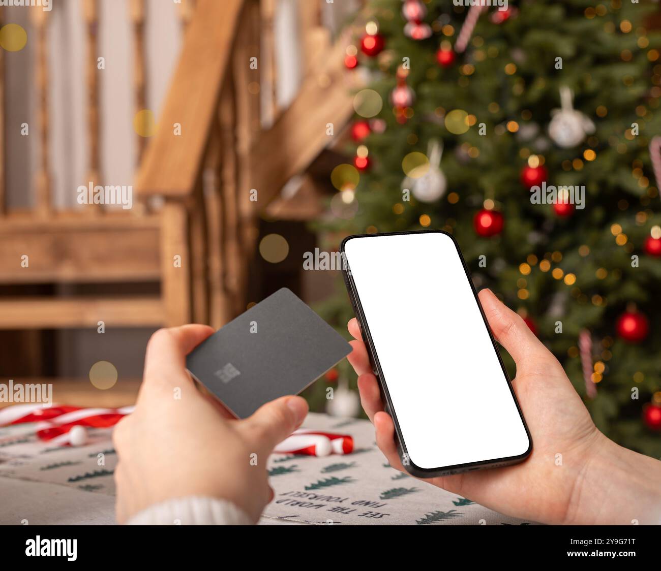 Con la mano che regge il mockup dello schermo del telefono cellulare, lo smartphone, le vacanze di Natale e la tecnologia. Pagamento in Internet con app bancaria e carta di credito. Foto Stock