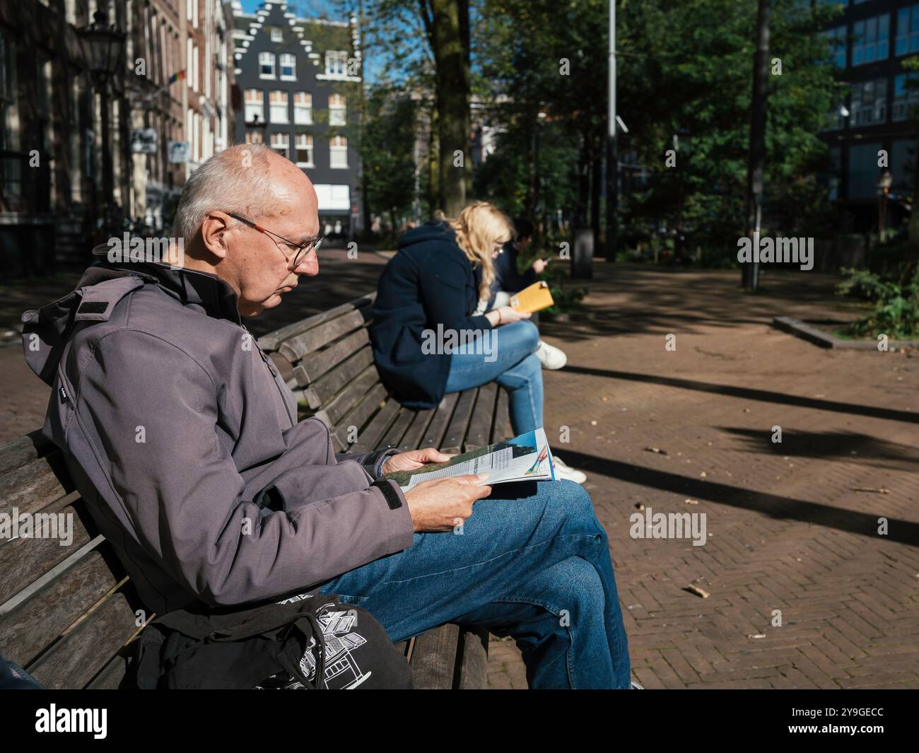 Persone sedute sulle panchine, leggono libri e si rilassano in una rara giornata di sole ad Amsterdam. Foto Stock