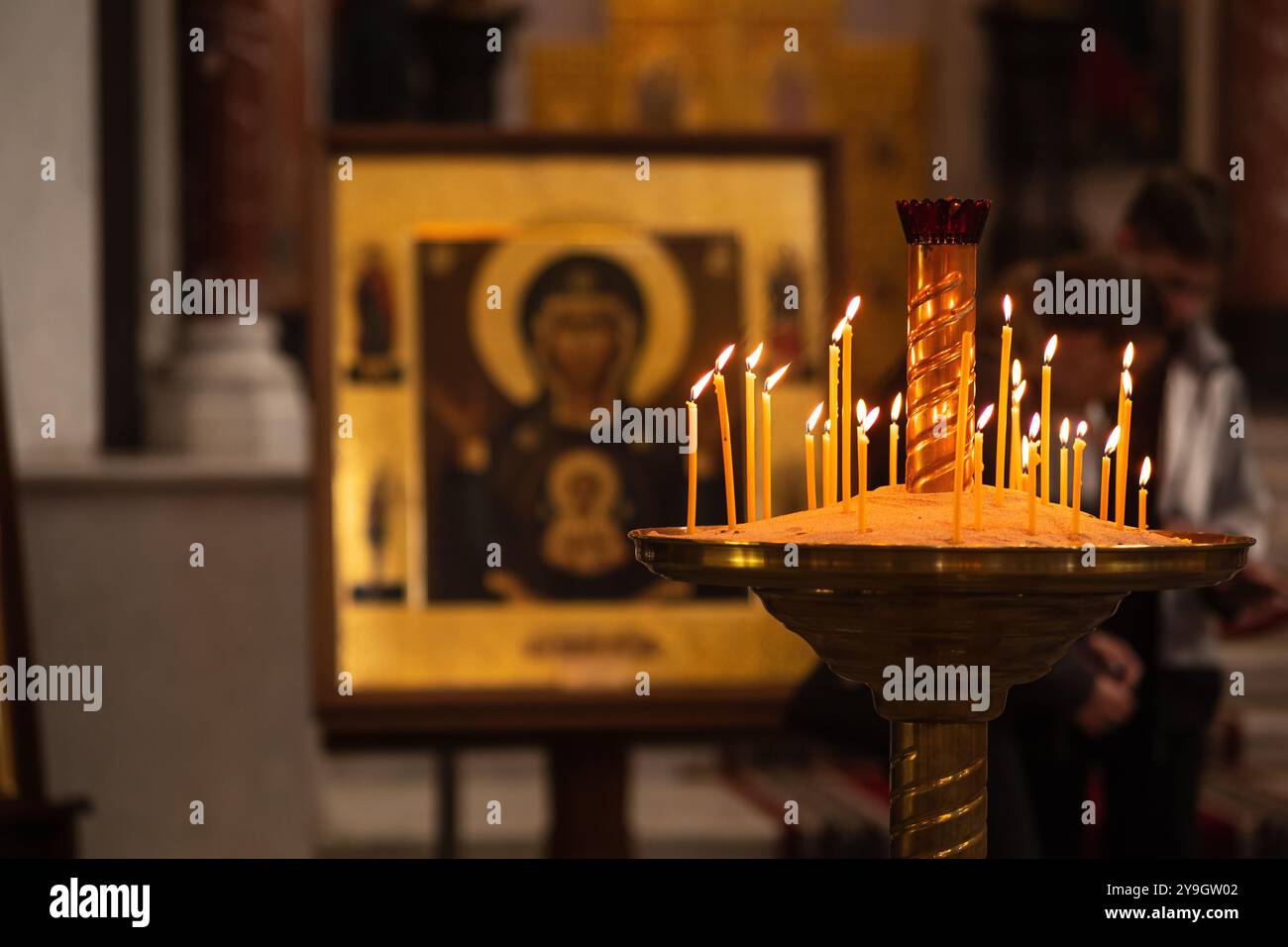 Kronstadt, Russia - 20 giugno 2024: Le candele bruciano in un candelabro in una stanza semi-buia di una chiesa ortodossa sullo sfondo di icone Foto Stock