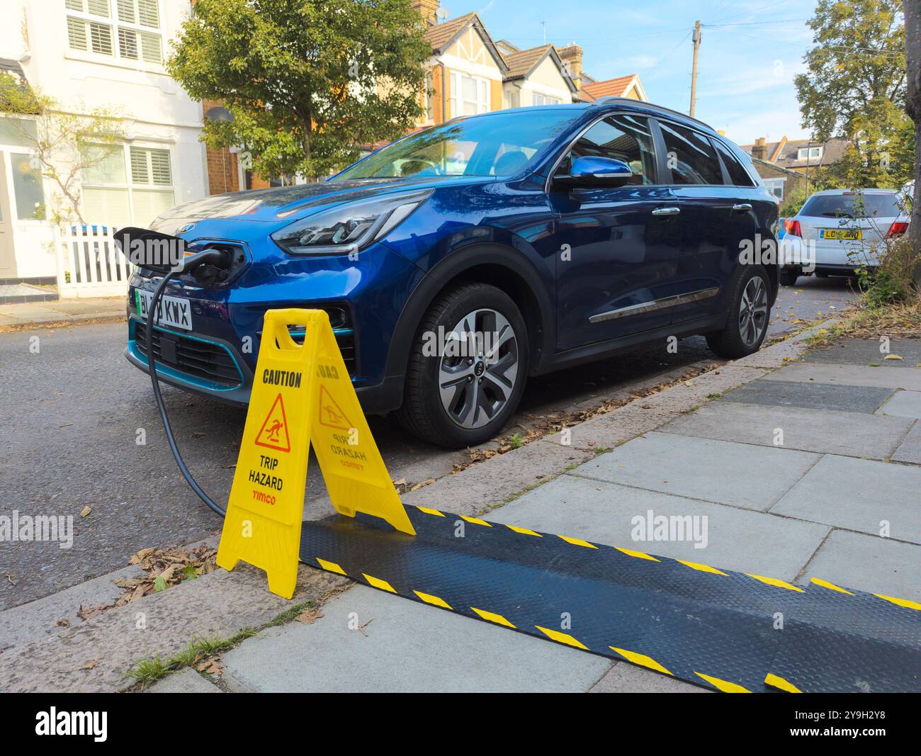 Ricarica di auto elettriche Kia in una strada residenziale da casa utilizzando protezioni per cavi marciapiede per il cavo di ricarica EV, Londra, Regno Unito Foto Stock