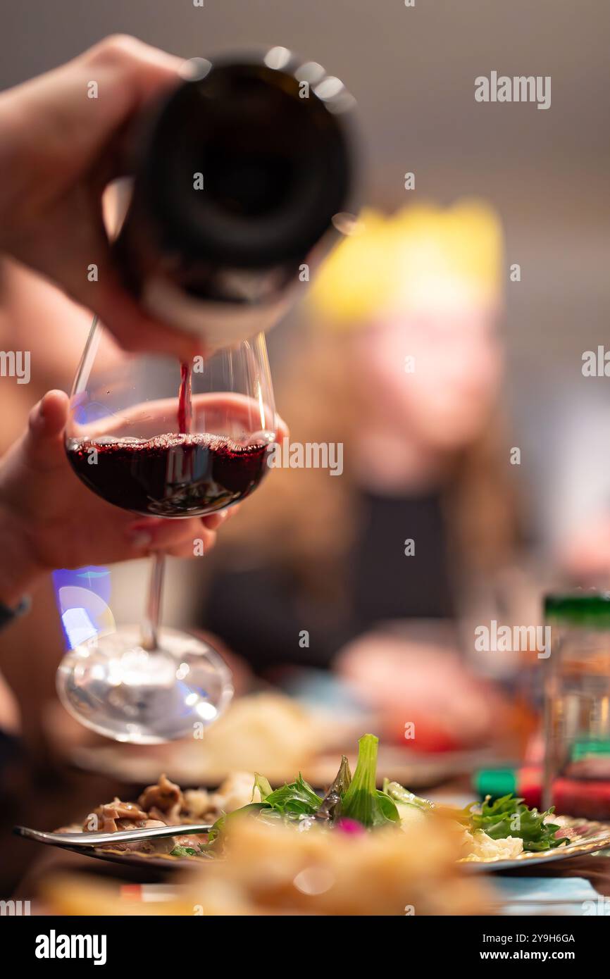 Un bicchiere di vino rosso che viene riempito da una bottiglia durante una cena di famiglia durante la stagione natalizia con vista ritratto. Foto Stock