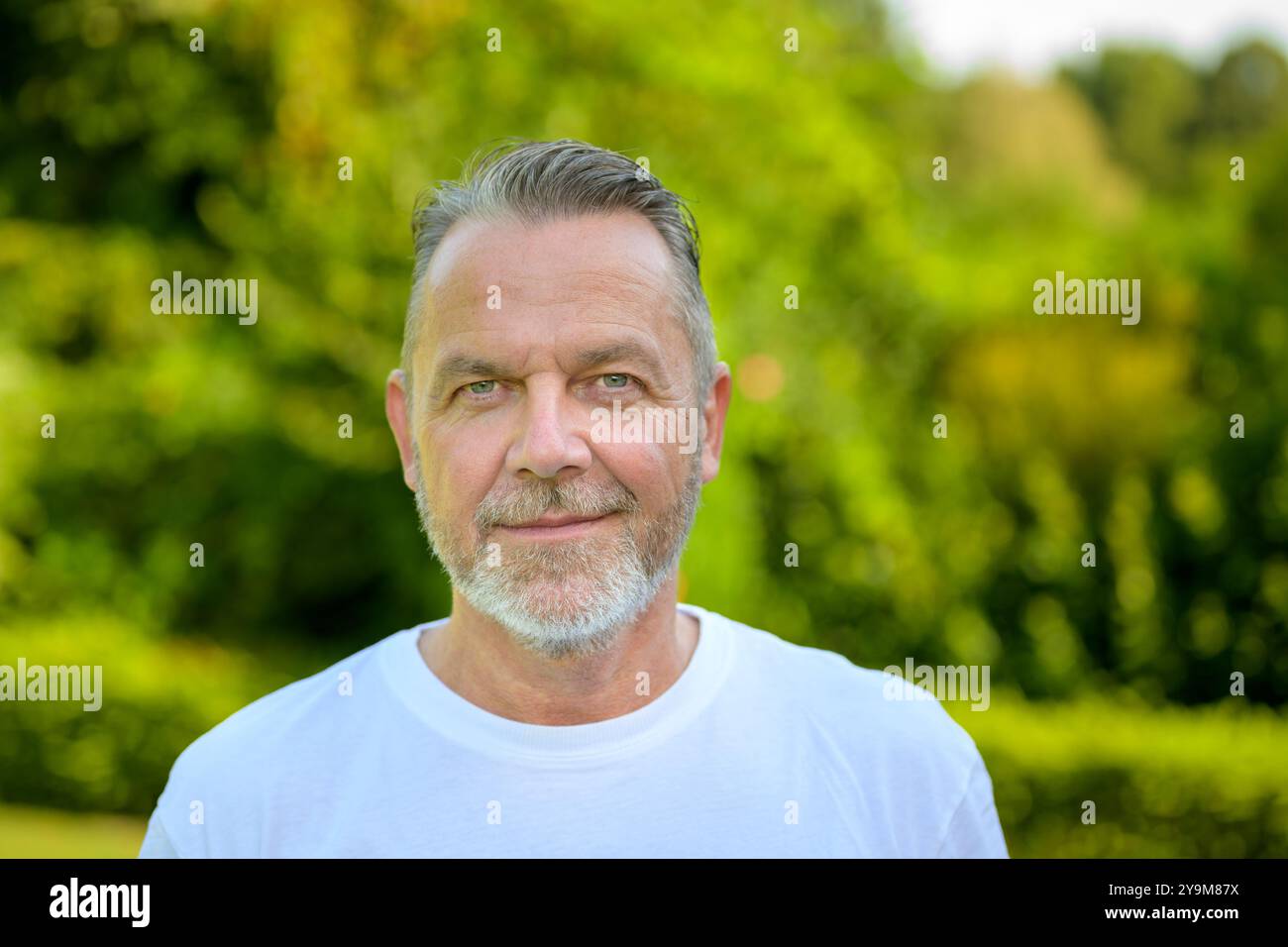 Ritratto di un uomo maturo con capelli grigi e barba corta, in piedi all'aperto e di fronte alla fotocamera. Foto Stock