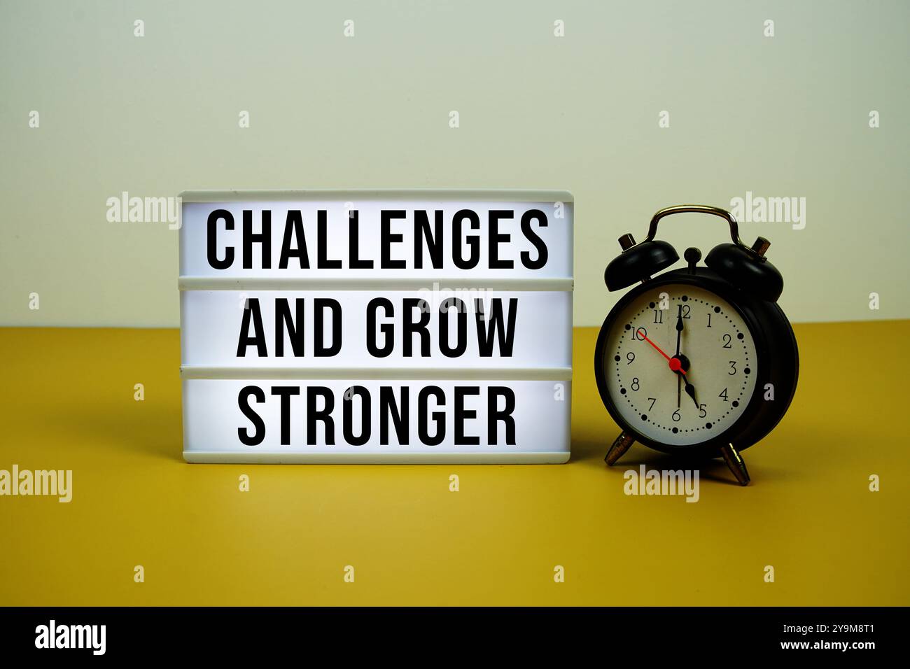Sfida e aumenta il testo su una scatola luminosa a LED con sveglia su sfondo giallo Foto Stock