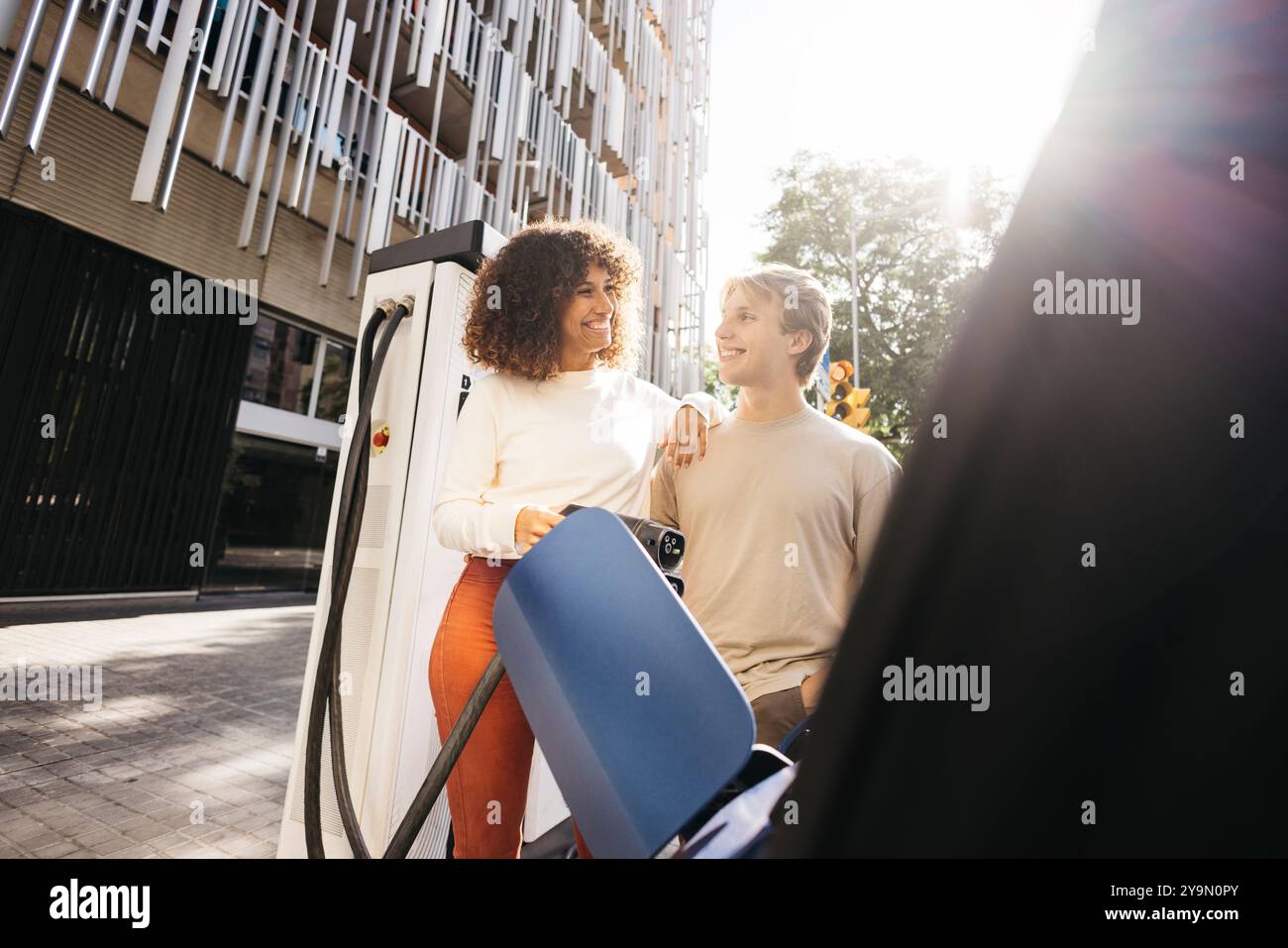 Coppia felice che ricarica la propria auto elettrica in una stazione all'aperto. Stile di vita urbano e trasporti ecologici. Impegnarsi in una vita sostenibile togeth Foto Stock