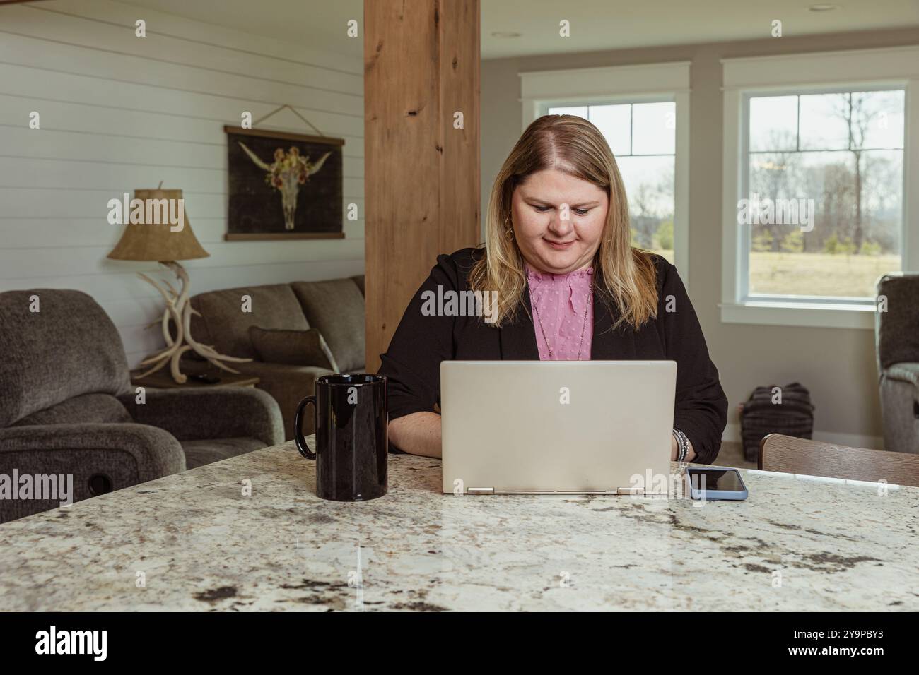 Donna che lavora su un notebook al bancone della cucina con una tazza da caffè Foto Stock