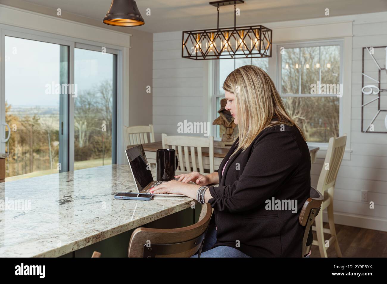 Donna che lavora su un notebook al bancone della cucina con una tazza da caffè Foto Stock