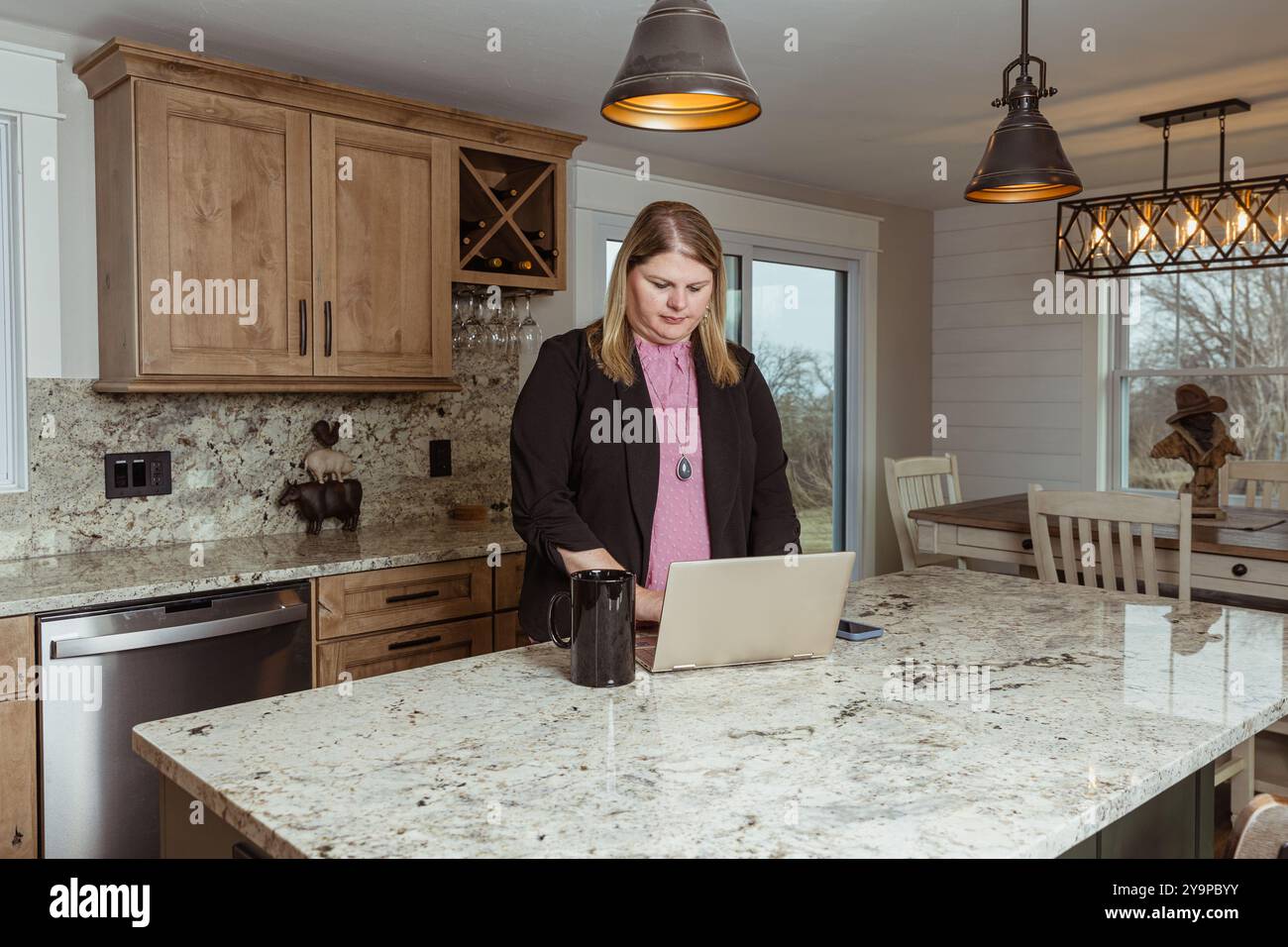Donna che lavora su un notebook al bancone della cucina con una tazza da caffè Foto Stock