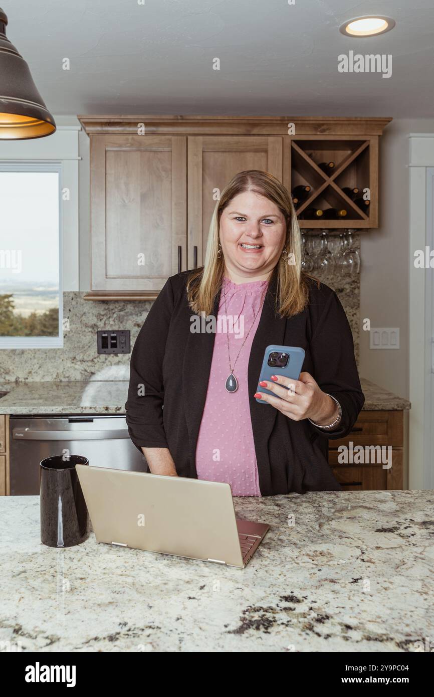 Donna che lavora su un notebook al bancone della cucina con una tazza da caffè Foto Stock
