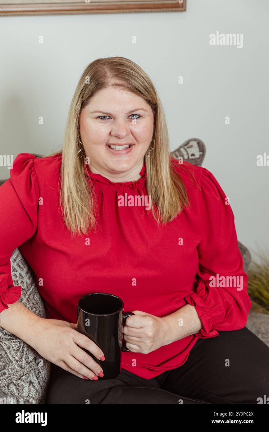 Donna con la parte superiore rossa seduta su una sedia, che tiene in mano una tazza da caffè Foto Stock