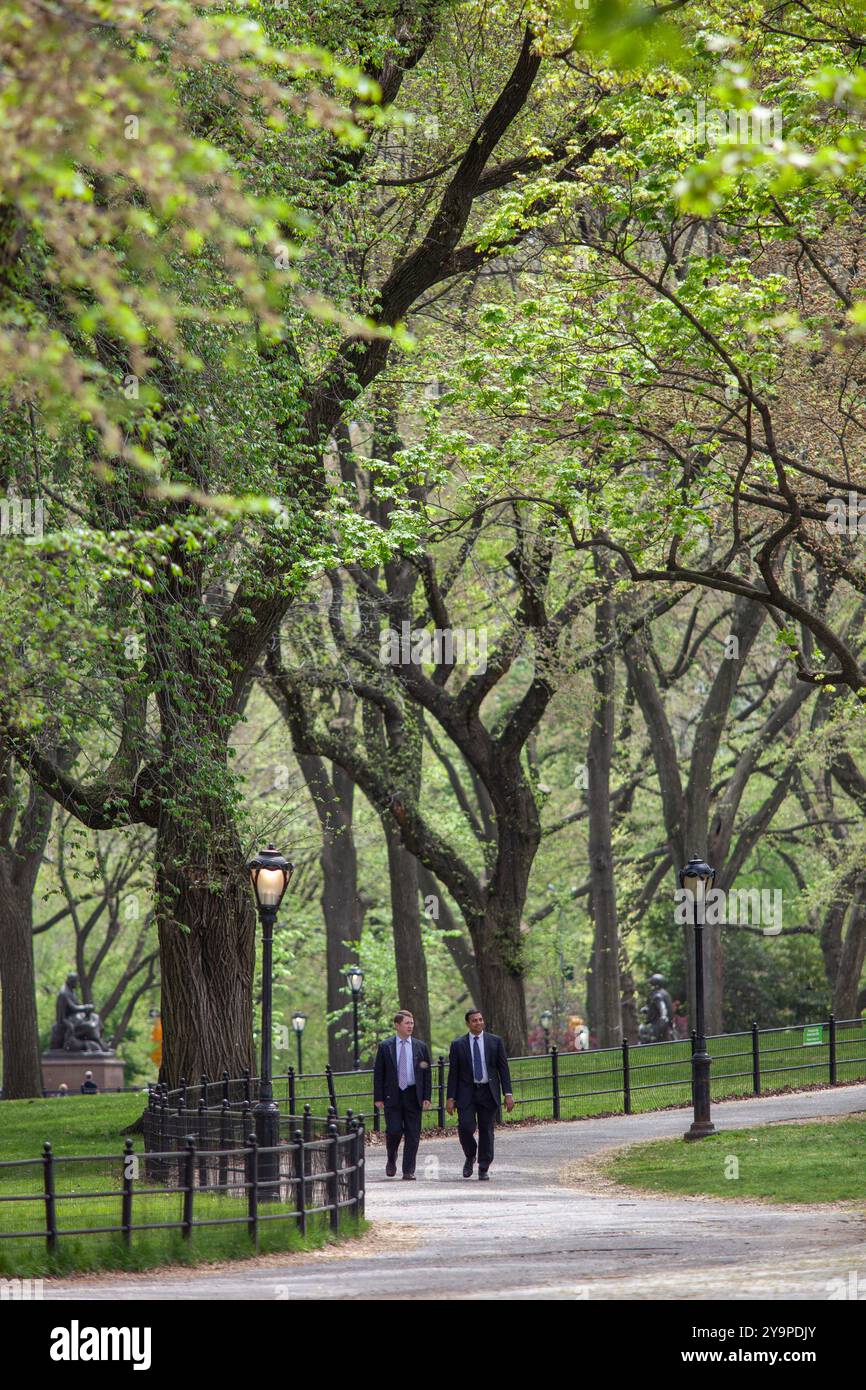 Uomini in abiti da lavoro che camminano attraverso il verde lussureggiante Central Park di New York Foto Stock