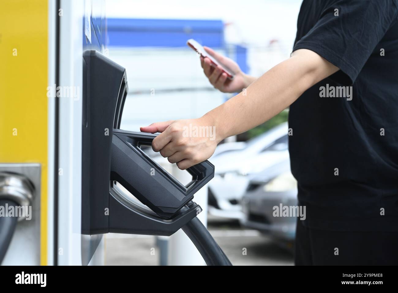 Giovane uomo che utilizza una stazione di ricarica per veicoli elettrici. Concetto di trasporto ecologico Foto Stock