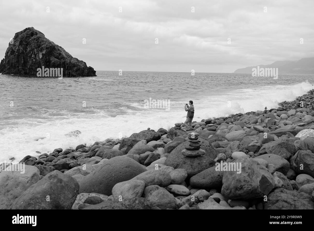 Turista che cattura la bellezza della costa rocciosa di Ilhéus da Janela e delle onde oceaniche sulla costa settentrionale dell'isola in bianco e nero Foto Stock