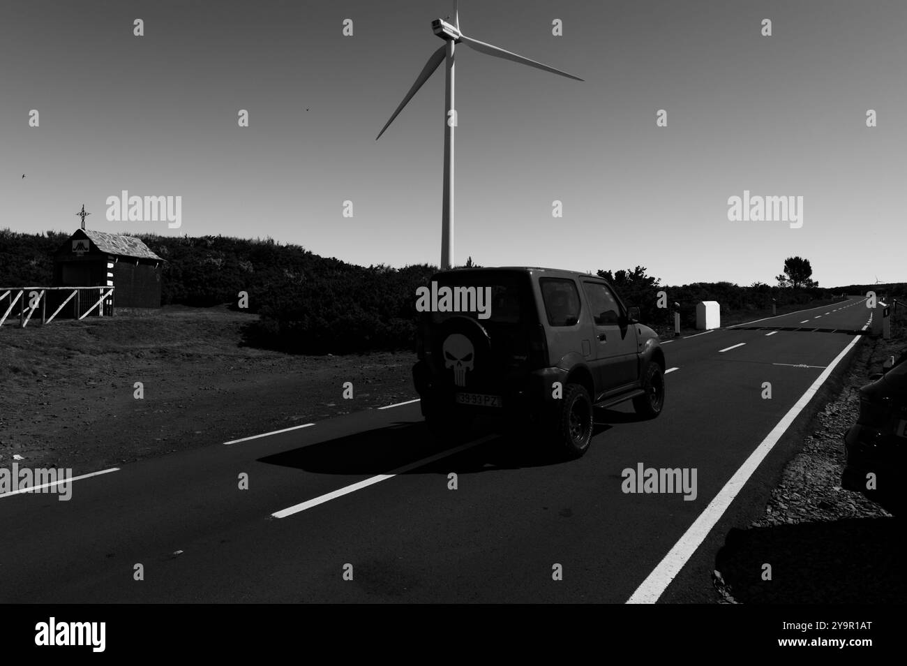 Veicolo fuoristrada che passa davanti a una turbina eolica e a una cappella su una tranquilla strada di madeira Foto Stock