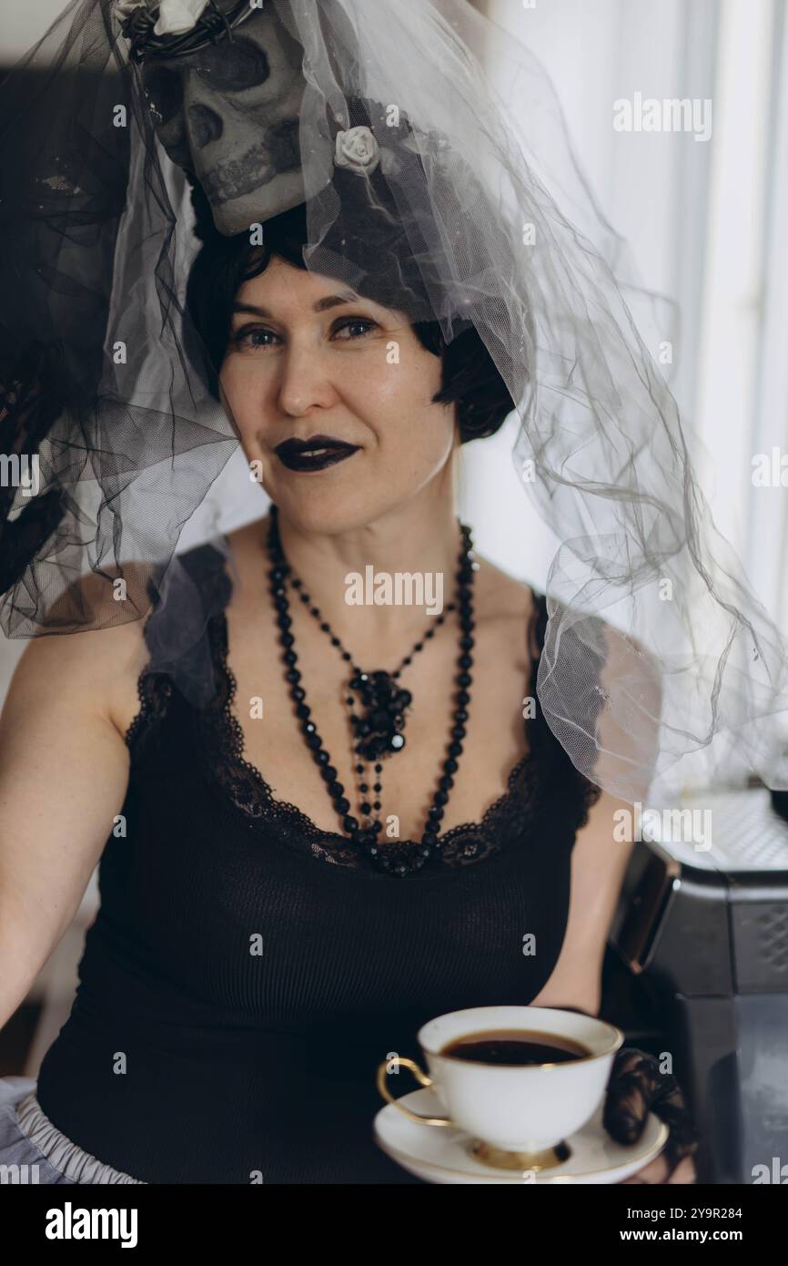 Donna in costume di Halloween che regge una tazza di caffè, sorride in un ambiente festoso e divertente. Foto di alta qualità Foto Stock