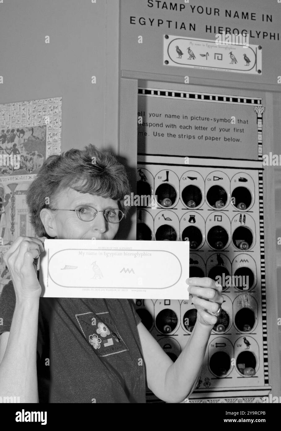 Donna caucasica di età compresa tra i 55 e i 60 anni è orgogliosa di possedere un biglietto che mostra il suo nome scritto in geroglifici egiziani presso il Museo dell'alfabeto di Waxhaw, NC. Foto Stock