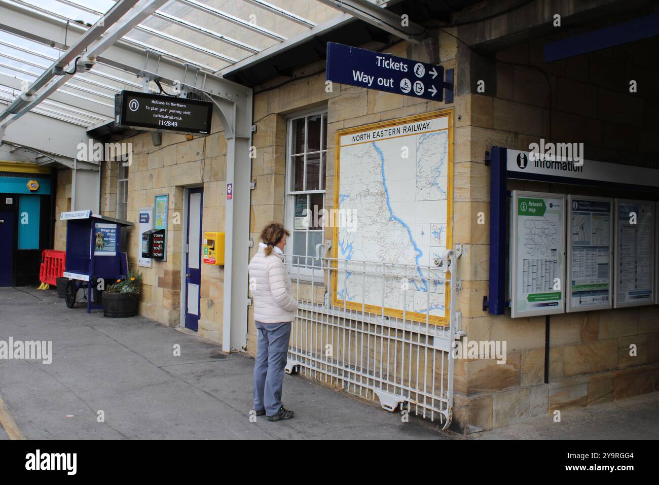 Giovane donna che guarda gli orari dei treni a Whitby, Inghilterra Foto Stock