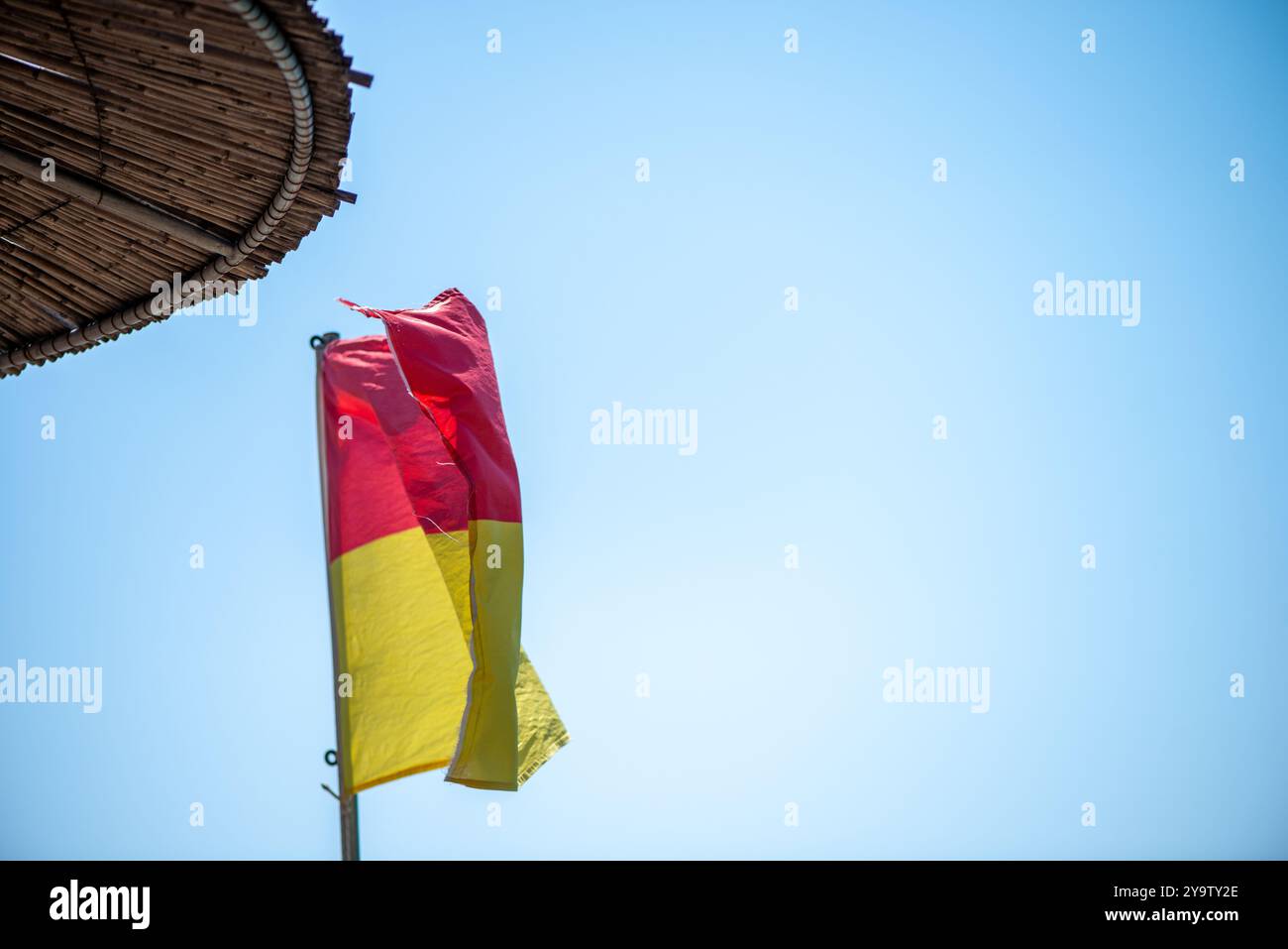 Un'immagine dinamica di una bandiera bagnino che sventola nel vento, simboleggia la sicurezza e la vigilanza sulla spiaggia, sullo sfondo di un cielo blu. Foto Stock