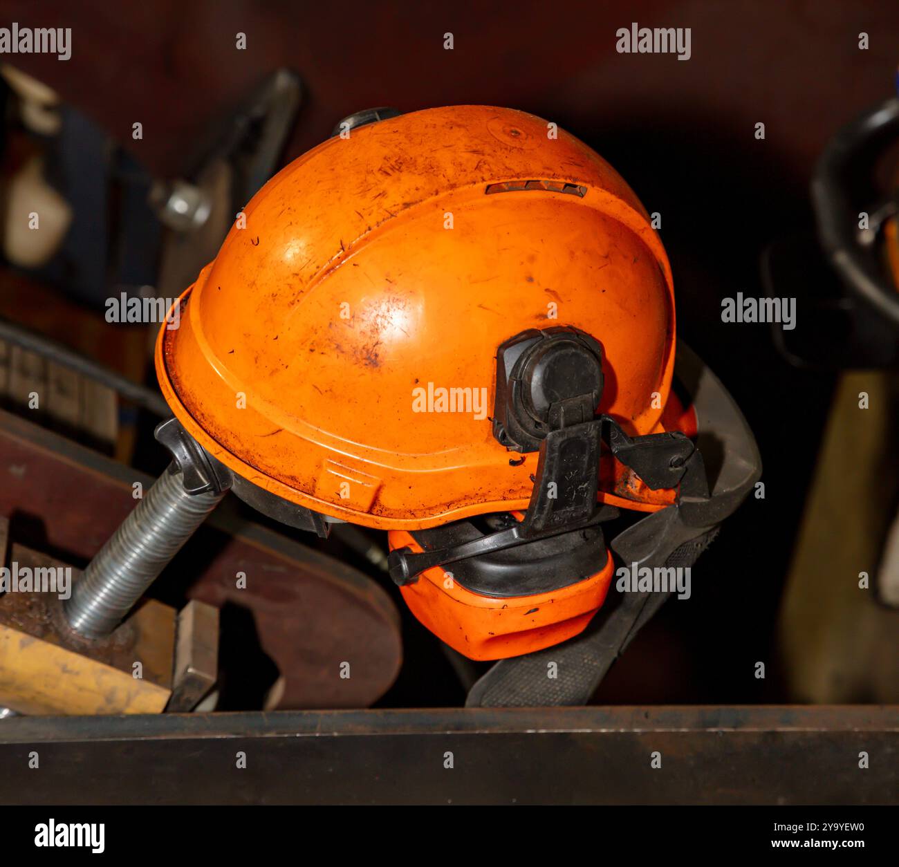 Fotografia di un elmetto di sicurezza arancione vecchio e sporco con protezione acustica appoggiato su un tavolo di metallo in un'officina. Foto Stock