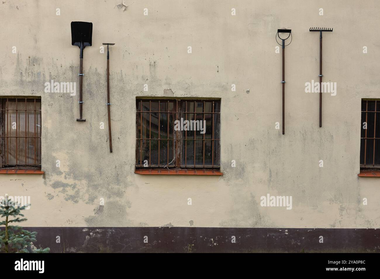 Vecchi utensili appesi su un muro di un edificio intempestivo con finestre sbarrate. Concetto di stile di vita rurale, attrezzature da giardinaggio e architettura vintage Foto Stock