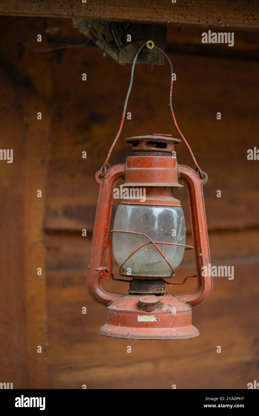 Lanterna rossa vintage in kerosene appesa su una trave di legno, che mostra fascino rustico e nostalgia. Concetto di illuminazione retrò, arredi antichi e attrezzature per esterni Foto Stock