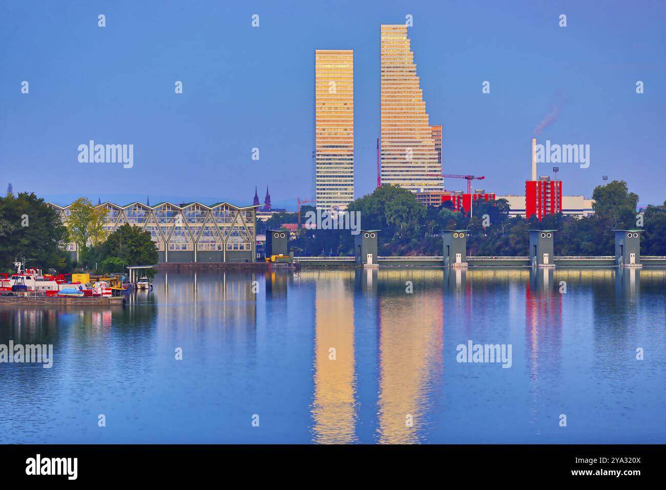 Grattacieli moderni che si riflettono nel fiume alla luce della sera accanto a uno sfondo urbano, Roche Towers, Hoffmann- la Roche, l'edificio più alto di Switze Foto Stock