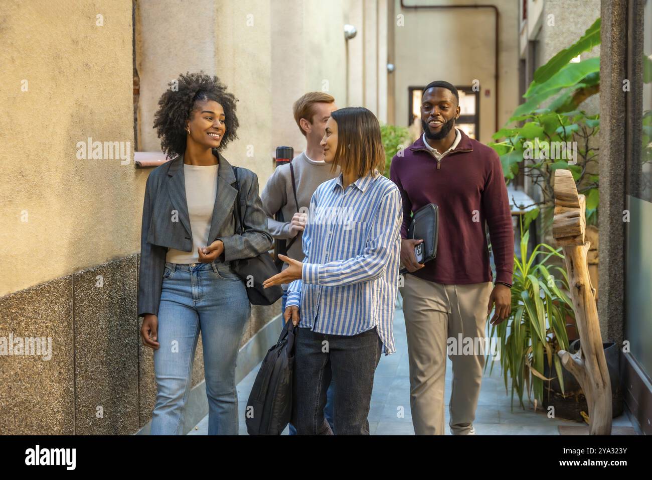 Gruppo di diversi colleghi maschi e femmine che escono dal coworking parlando e sorridendo Foto Stock