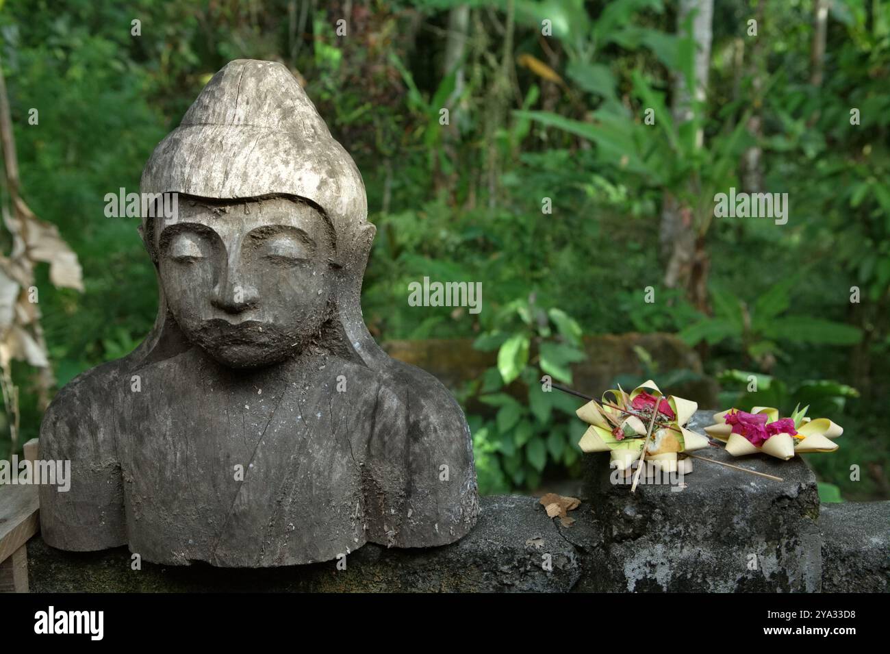 Offerta spirituale balinese accanto a una scultura in legno nel villaggio Pakudwi, Gianyar, Bali, Indonesia. Foto Stock