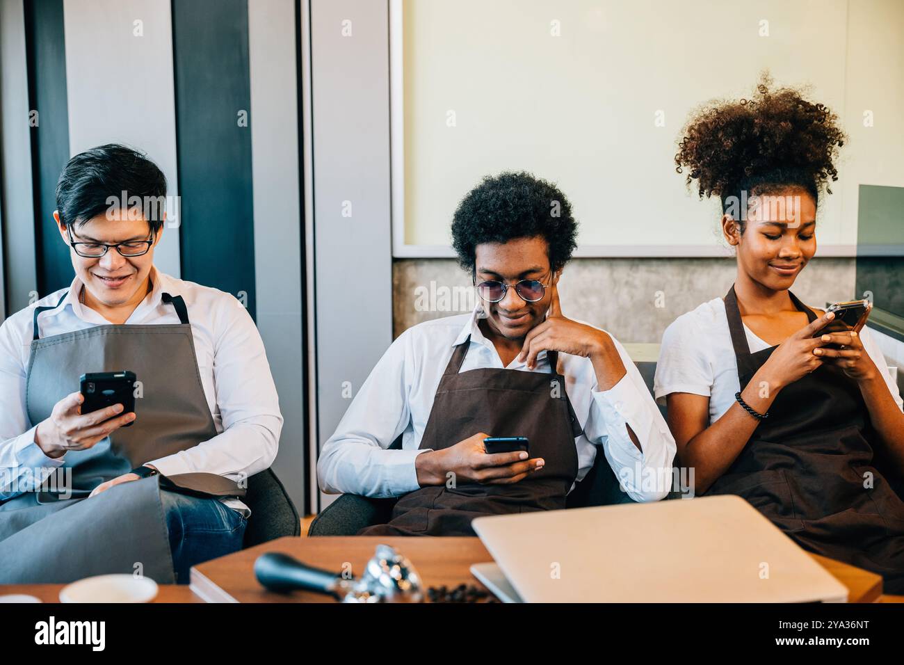 Un gruppo diversificato di baristi si è riunito in un bar utilizzando il telefono per rilassarsi. Professionisti in Foto Stock