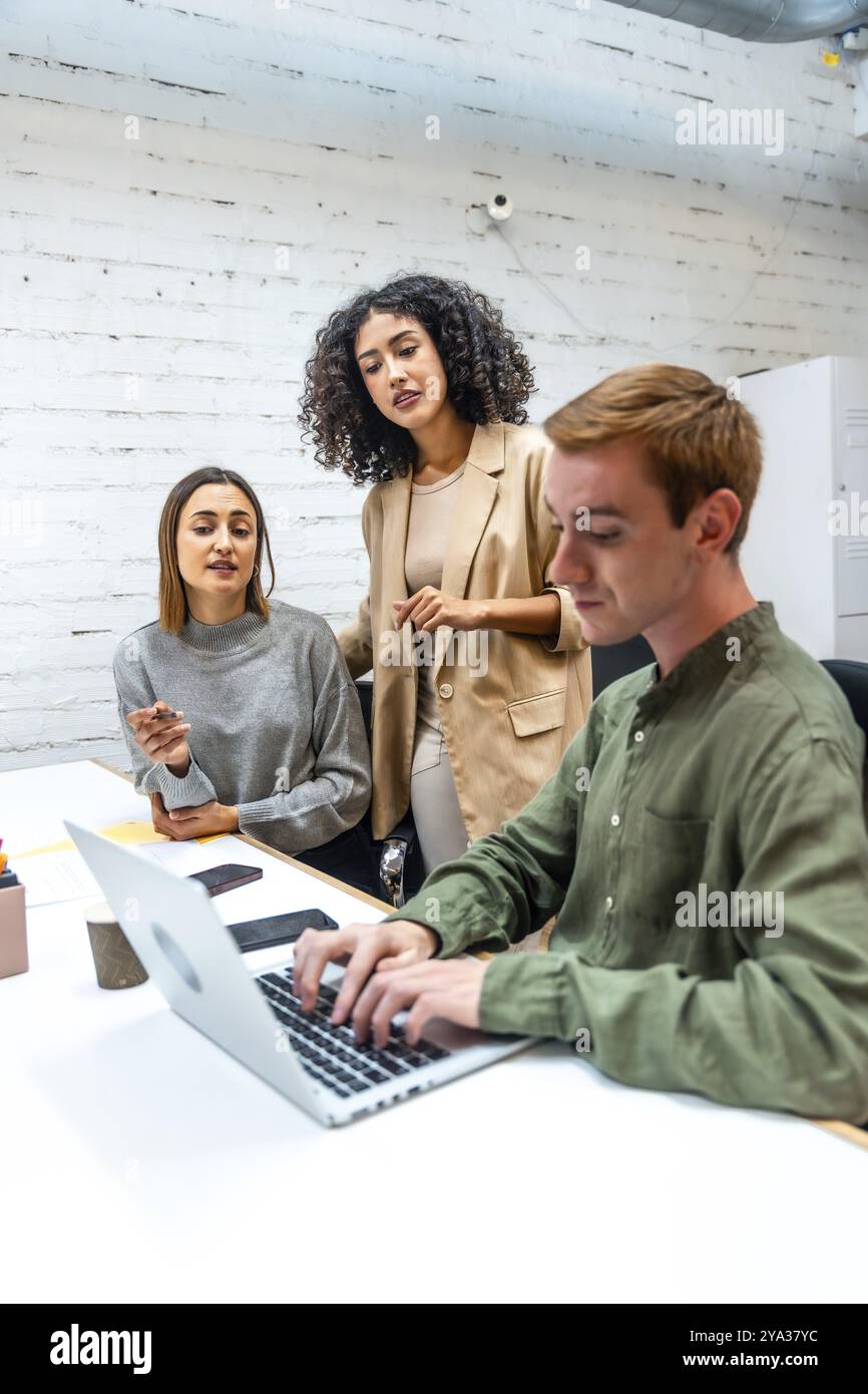 Foto verticale di tre diversi colleghi che utilizzano un laptop e discutono in una stanza di coworking Foto Stock