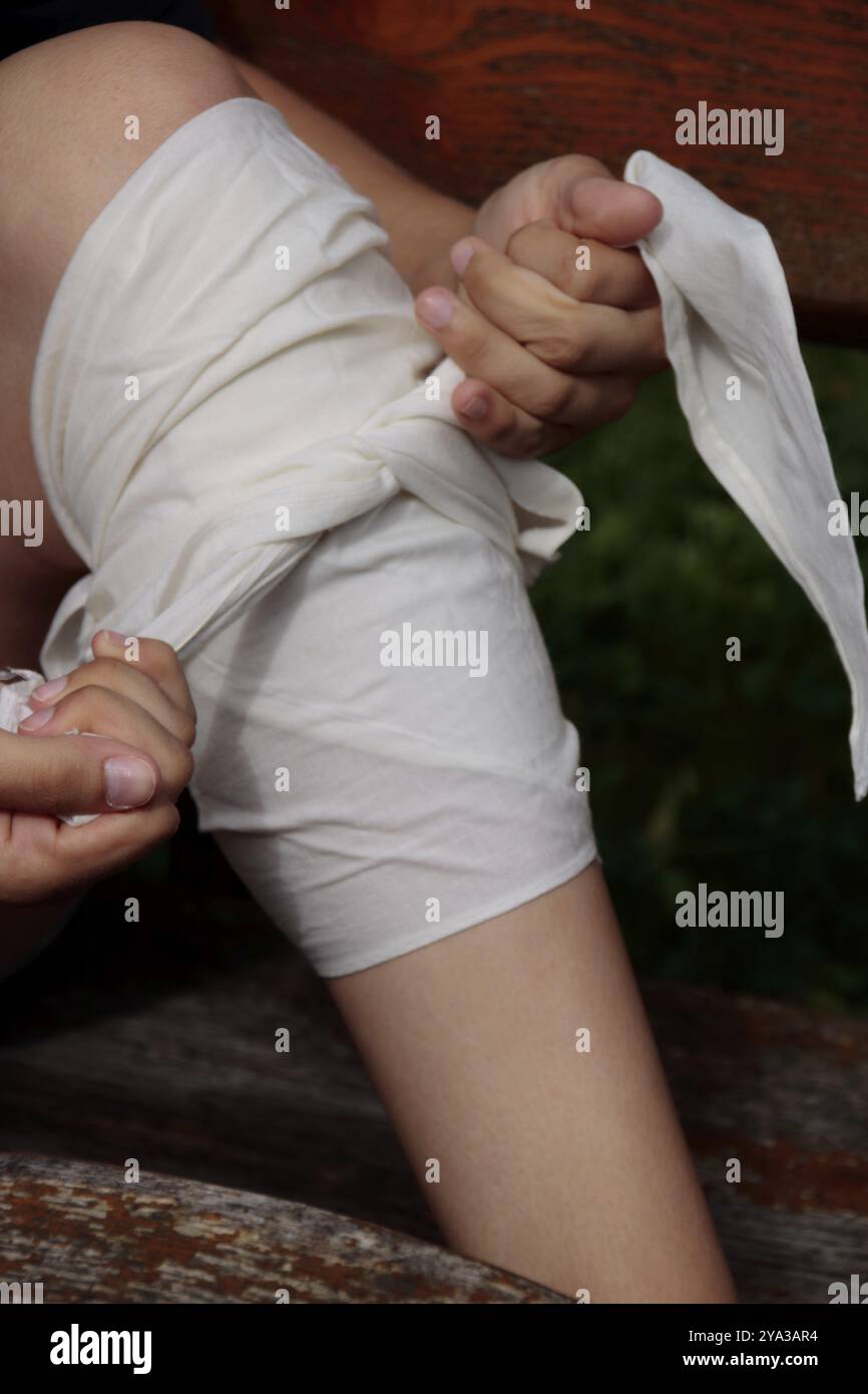 Una bendatura a pressione viene applicata sotto un ginocchio con un panno triangolare Foto Stock