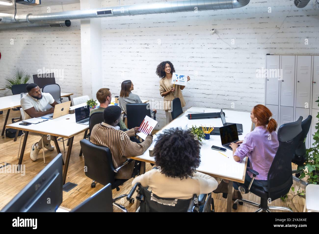 Donna che mostra grafici e dati durante l'incontro di coworking con diversi giovani in un moderno spazio di coworking Foto Stock