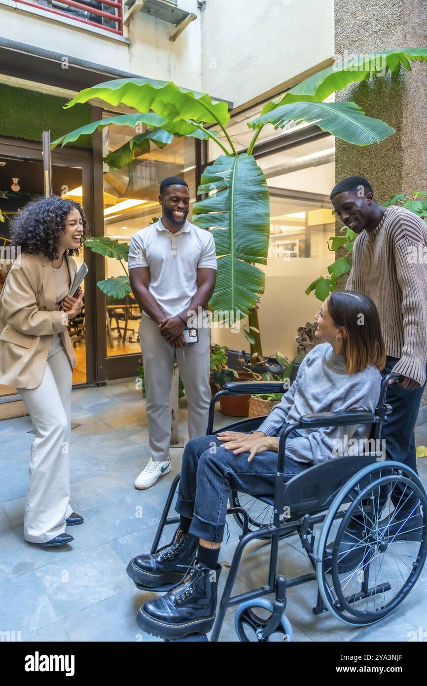 Colleghi diversi e felici che chiacchierano all'ingresso dell'ufficio con una donna disabile con sedia a rotelle Foto Stock