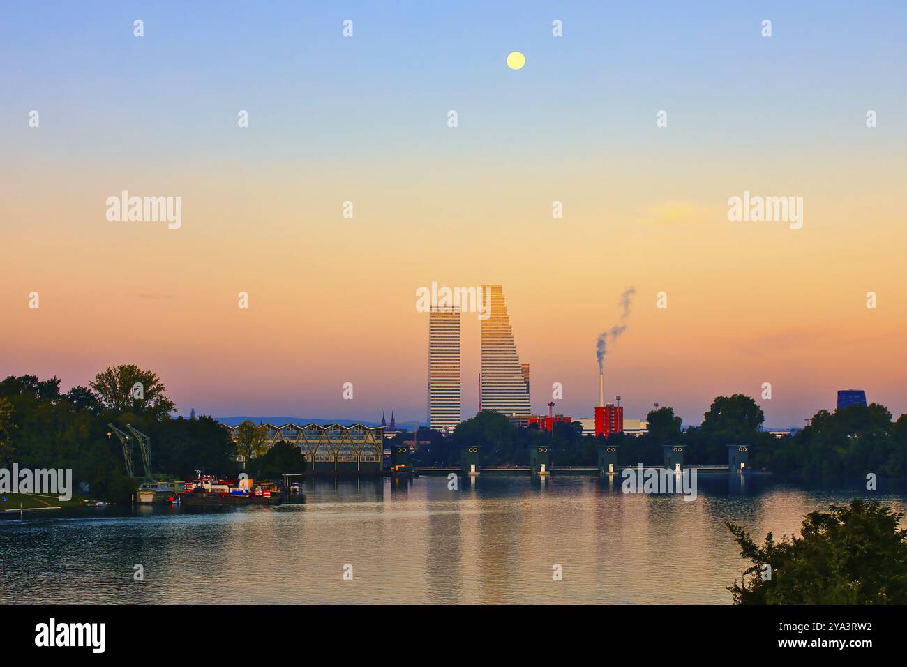 Paesaggio fluviale al tramonto con grattacieli e luna piena. La scena contiene accenti naturali e industriali, Roche Towers, Hoffmann- la Roche, le più alte Foto Stock