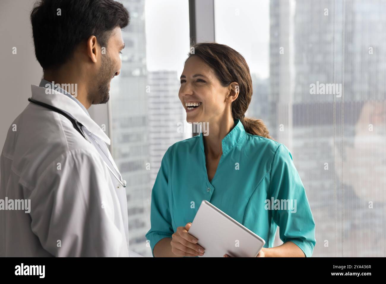 Una giovane infermiera sorridente chiacchiera con un medico di sesso maschile per finestra Foto Stock