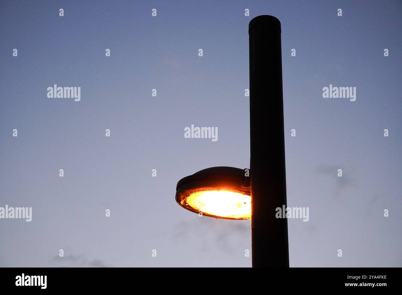 Una luce stradale illuminata in prima serata, che illumina il cielo al crepuscolo con un soffice bagliore, creando un'atmosfera tranquilla e urbana. Foto Stock
