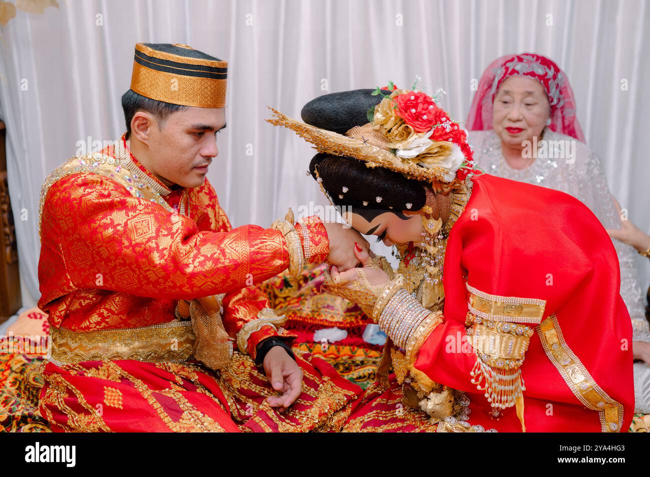 Coppia asiatica indonesiana che indossa abiti tradizionali e bacia la mano dello sposo, tradizione Bugis, Sulawesi meridionale. Indonesia. Foto Stock