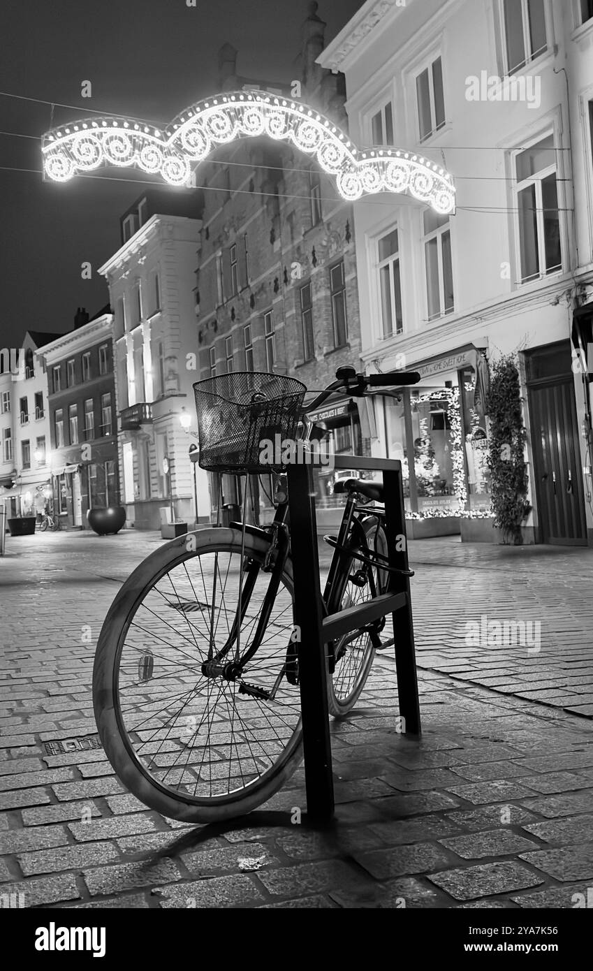 “Una notte tranquilla in città, con una bicicletta solitaria appoggiata su strade acciottolate sotto luci festose.” Foto Stock