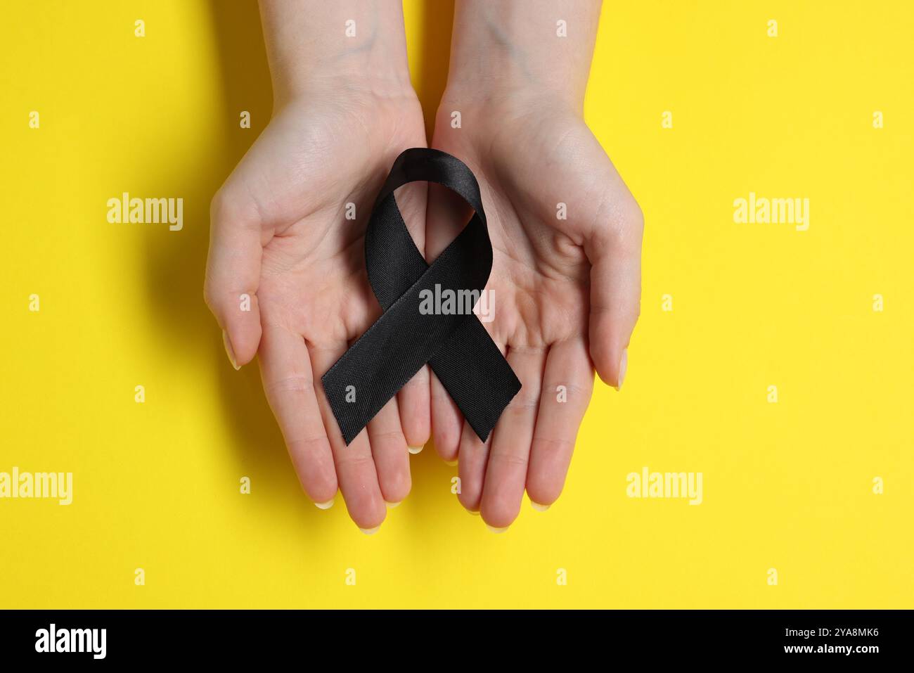 Donna con nastro nero su sfondo giallo, vista dall'alto. Concetto di melanoma e lutto Foto Stock