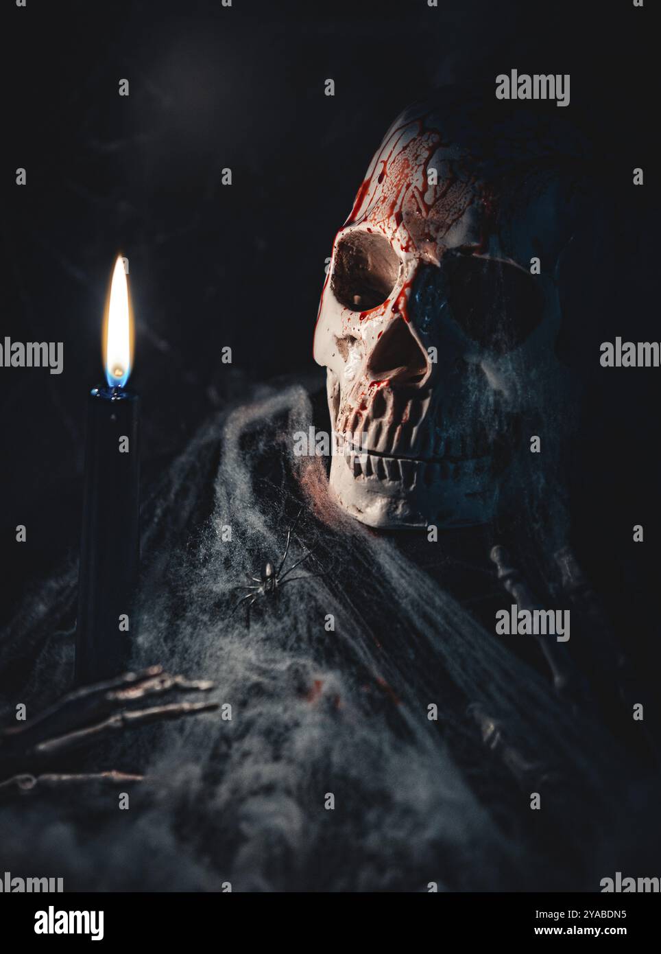 Cranio con tracce di sangue e ragnatele, accanto a una candela in un ambiente buio Foto Stock