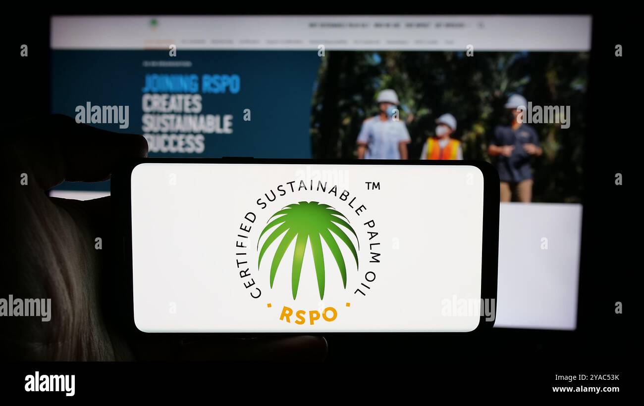 Persona che detiene un cellulare con il logo Roundtable on Sustainable Palm Oil (RSPO) sullo schermo davanti alla pagina Web. Mettere a fuoco il display del telefono. Foto Stock