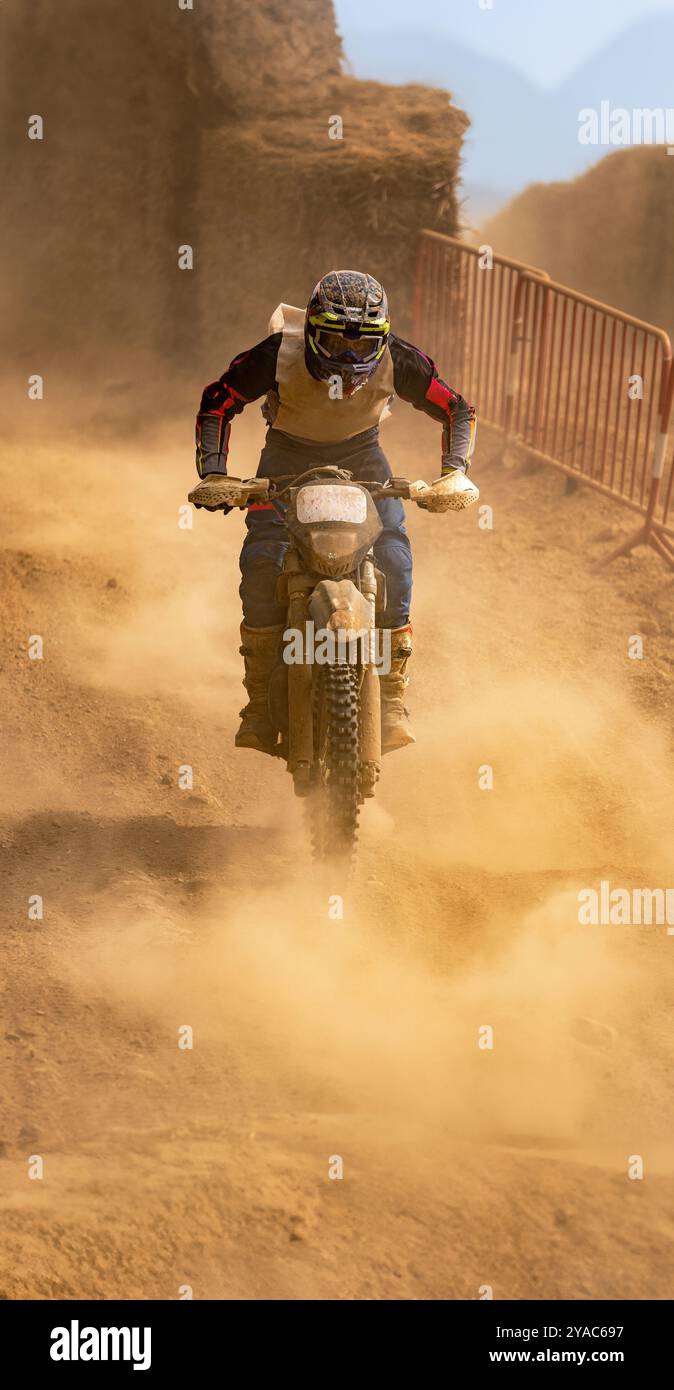 Pilota di motocross in azione che corre lungo una ripida pendenza circondata da un terreno polveroso in una gara di resistenza. Foto Stock