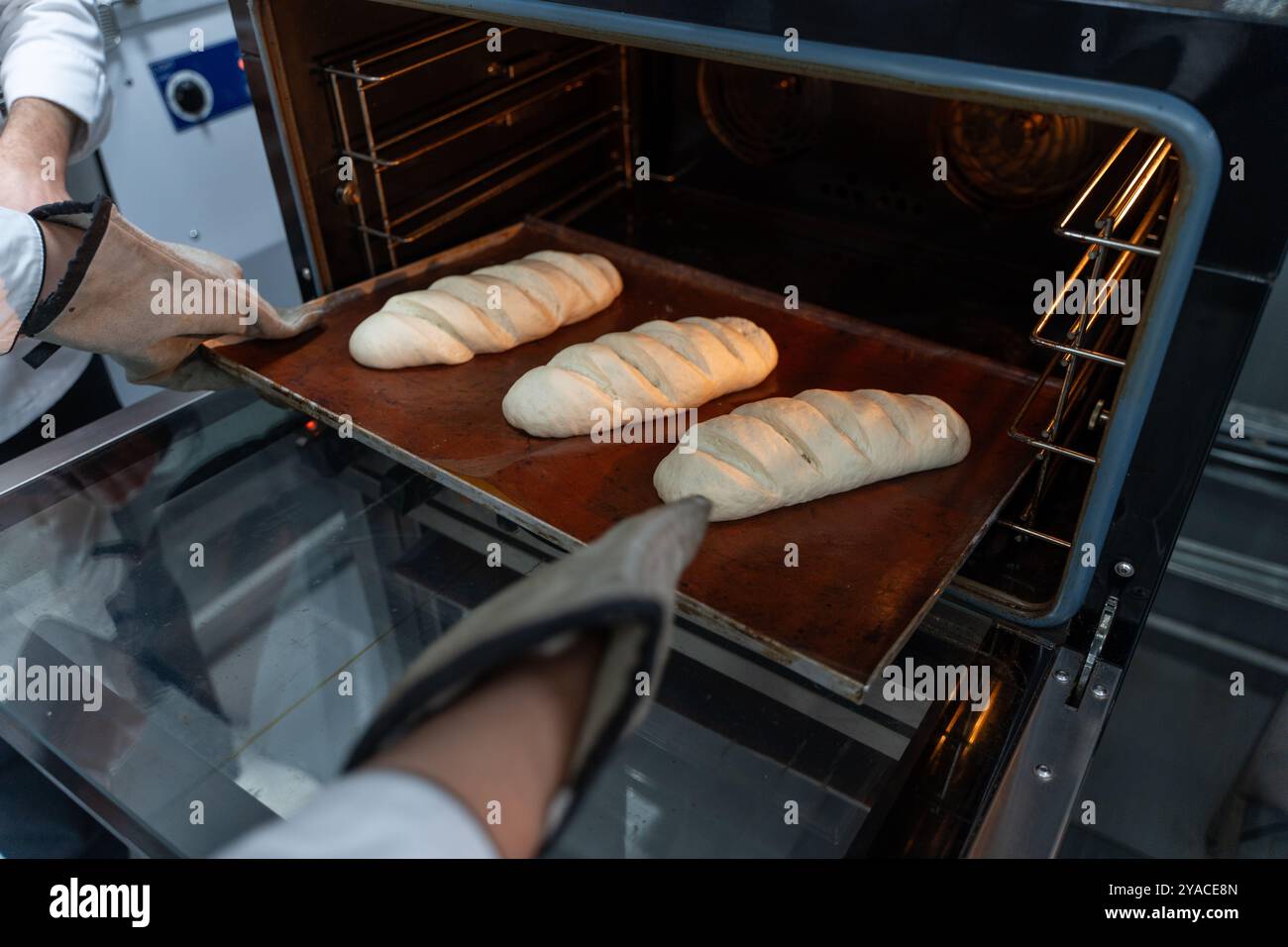Il fornaio mette i pani di pane nel forno. Preparare il pane in una piccola panetteria. Foto di alta qualità Foto Stock