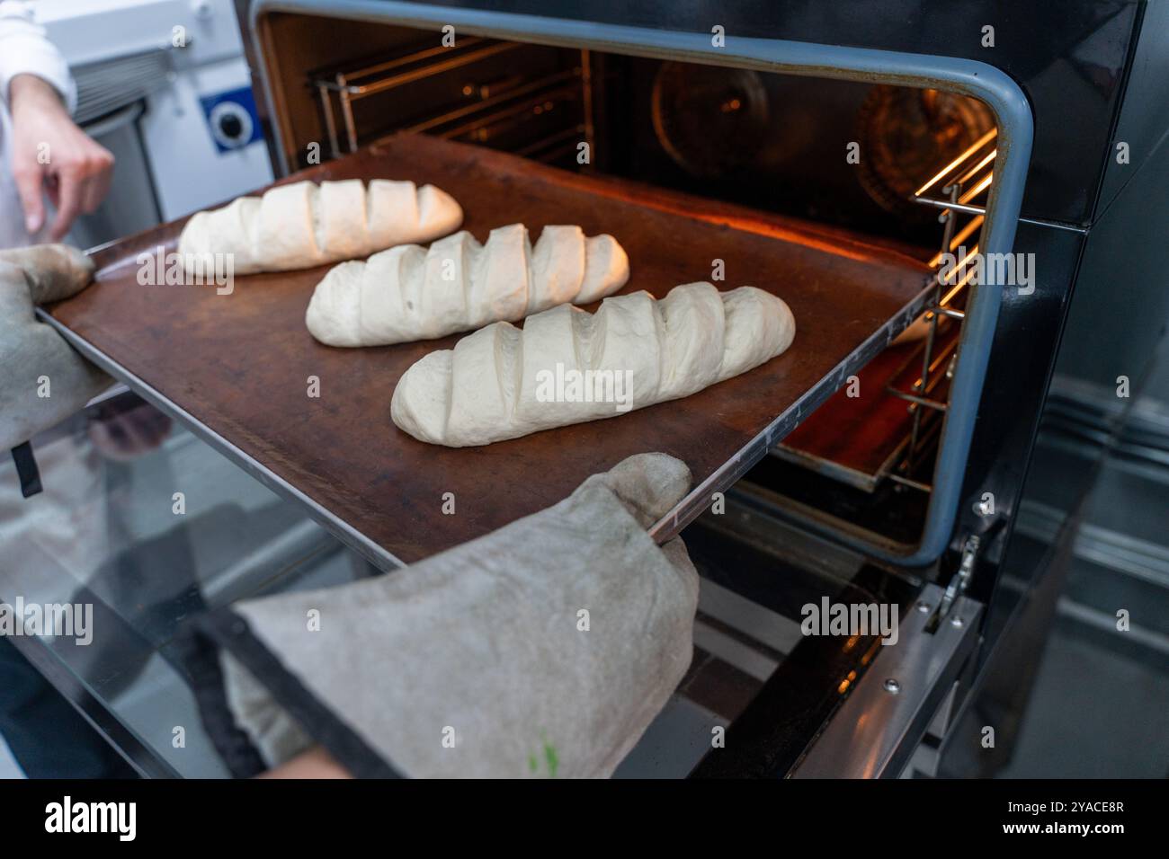 Il fornaio mette i pani di pane nel forno. Preparare il pane in una piccola panetteria. Foto di alta qualità Foto Stock