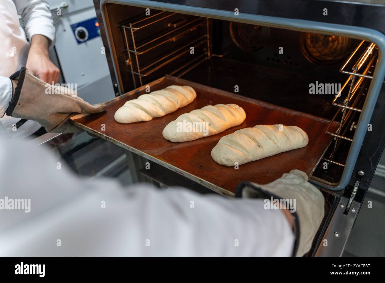 Il fornaio mette i pani di pane nel forno. Preparare il pane in una piccola panetteria. Foto di alta qualità Foto Stock