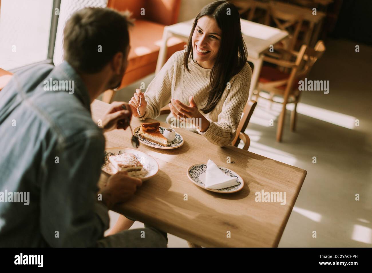 In un caffè caldo e invitante, una coppia condivide risate e deliziose prelibatezze, assaporando caffè e pasticcini mentre si crogiola al sole del pomeriggio. Foto Stock