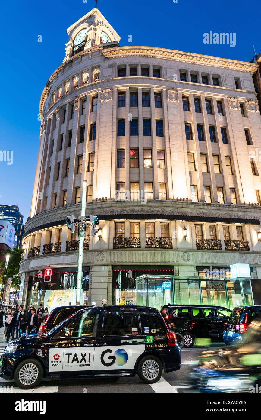 La famosa casa Seiko di Ginza, formalmente l'edificio Wako, illuminata di sera, mentre di fronte passano taxi e auto. Notte. Foto Stock