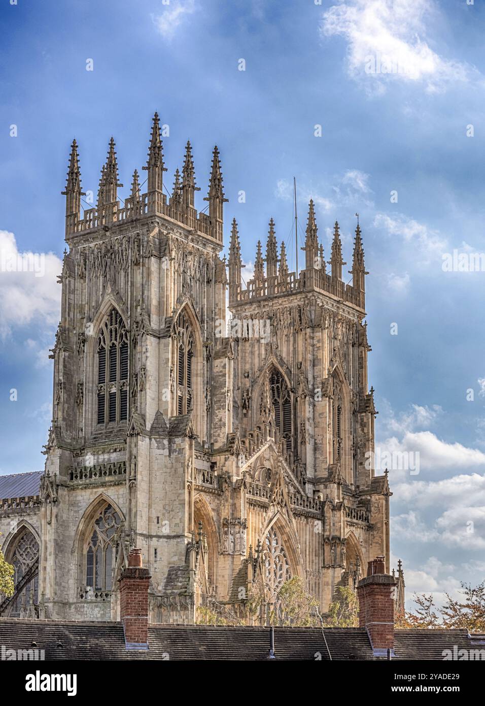 Le torri occidentali della York Minster contro un cielo nuvoloso visto dalle mura della città. Ci sono camini e alberi in primo piano. Foto Stock