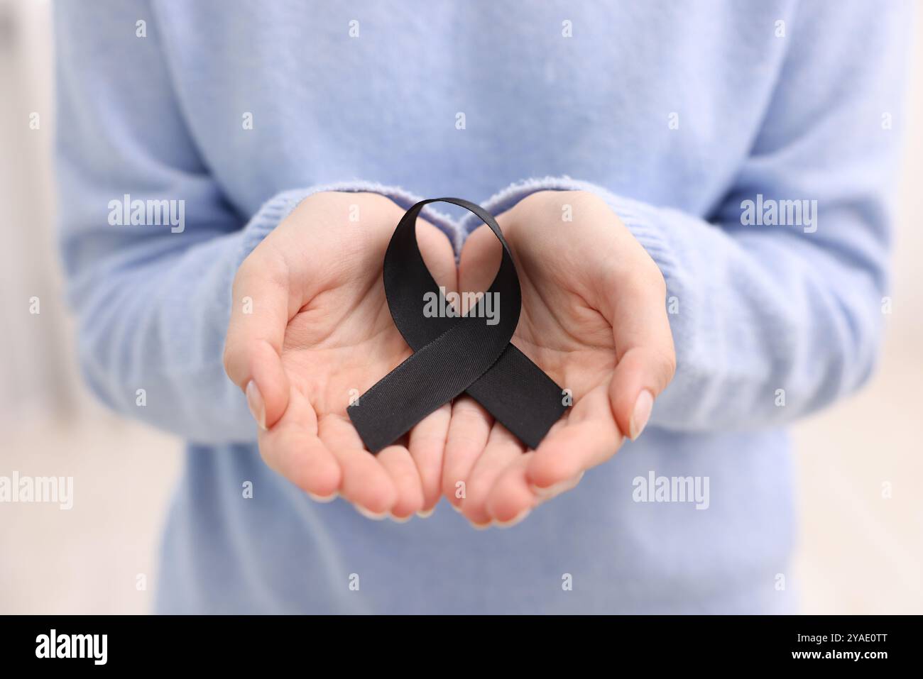 Donna con nastro nero su sfondo chiaro, primo piano. Concetto di melanoma e lutto Foto Stock