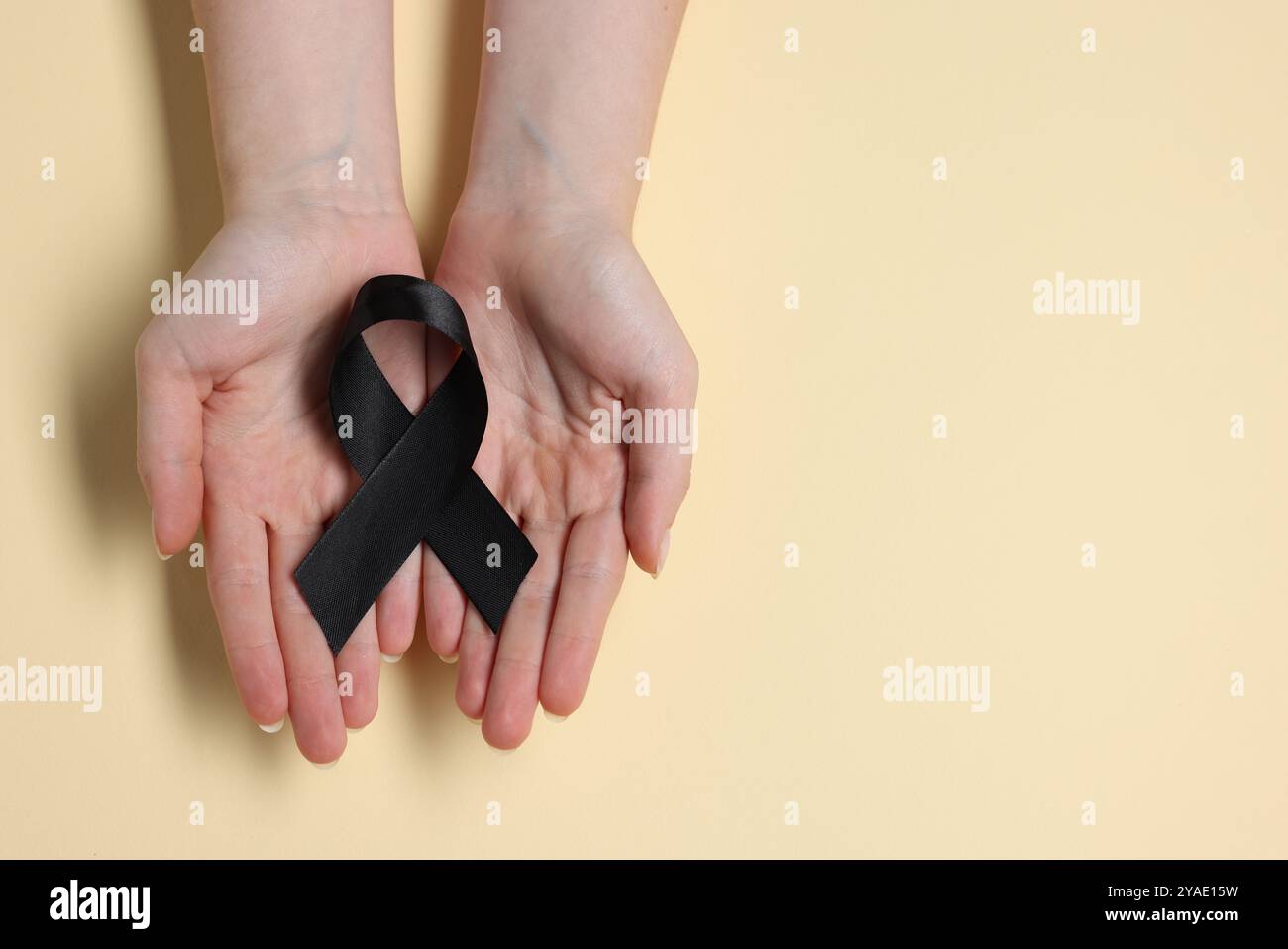 Donna con nastro nero su sfondo beige, vista dall'alto con spazio per il testo. Concetto di melanoma e lutto Foto Stock